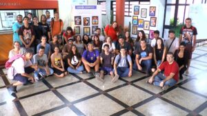 Estudantes de Design Gráfico do UNIVEM posando ao lado de uma exposição de seus trabalhos no campus.